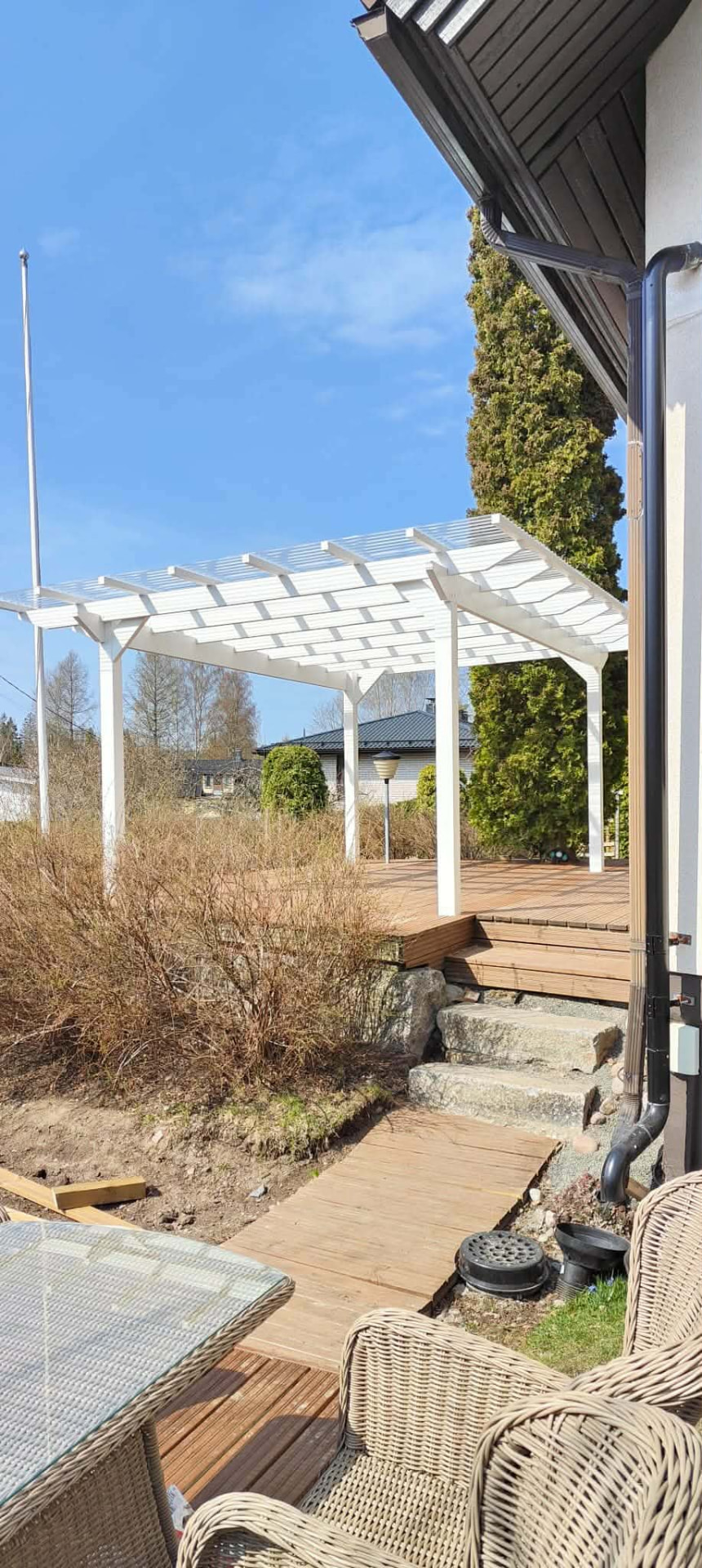 Valkoinen pergola ja puuterassi pihalla.